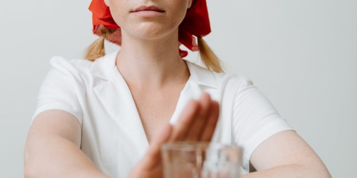 Ein Frau mit Kopftuch sitzt am Tisch und hält die Hand vor ein Glas Alkohol