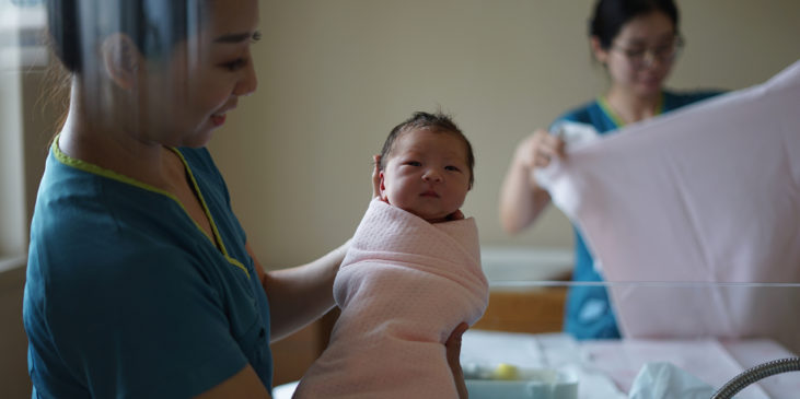 Eine Hebamme hält ein neugeborenes Baby im Arm