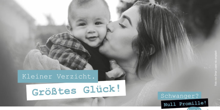 Ein kleines Baby von vorne das von seiner dunkelhaarigen Mama auf die Backe geküsst wird