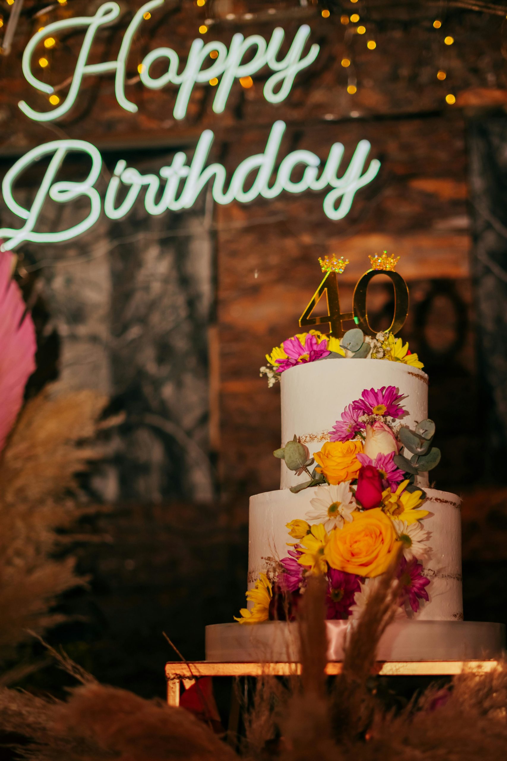 Zweistöckige Sahnetorte mit bunten Blüten und goldenen Kerzen mit den Zahlen 40 verziert
