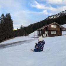 Winteridylle: Kleinkind spielt im Schnee vor einer Berghütte.