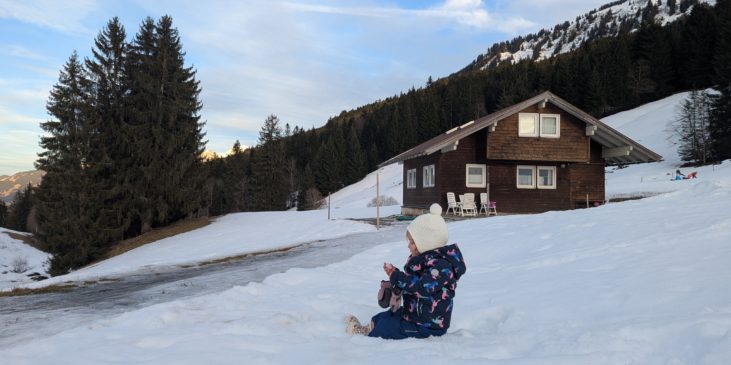 Winteridylle: Kleinkind spielt im Schnee vor einer Berghütte.