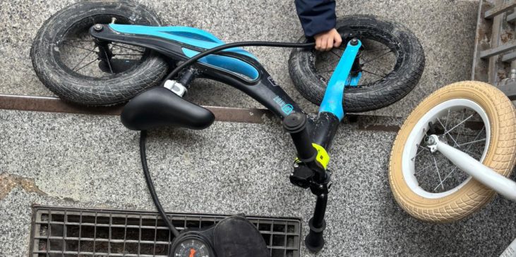 Kind mit Laufrad und Mama pumpt Luft rein