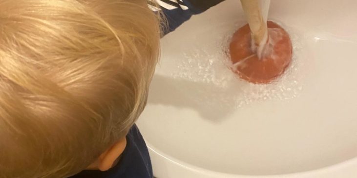 Draufsicht auf Kind mit Pömpel an laufendem Waschbecken