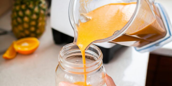 Orangefarbener Smoothie wird in ein Glas gekippt