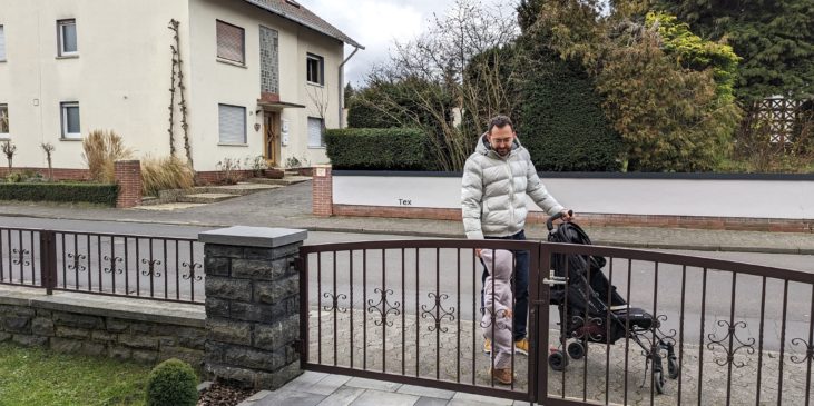 Vater mit Kind und Kinderwagen vor dem Hof-Tor