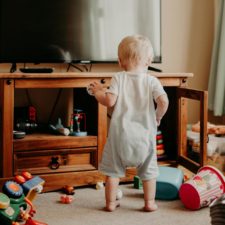 Kleinkind steht im Wohnzimmer zwischen verstreutem Spielzeug – typischer Alltag mit Baby und Spielchaos