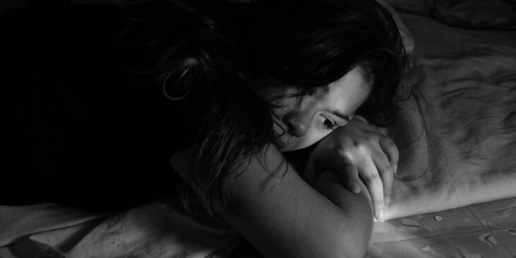 Schwarz-weiß Foto einer Frau, die traurig auf dem Bett liegt, mit dem Kopf auf ihren verschränkten Armen