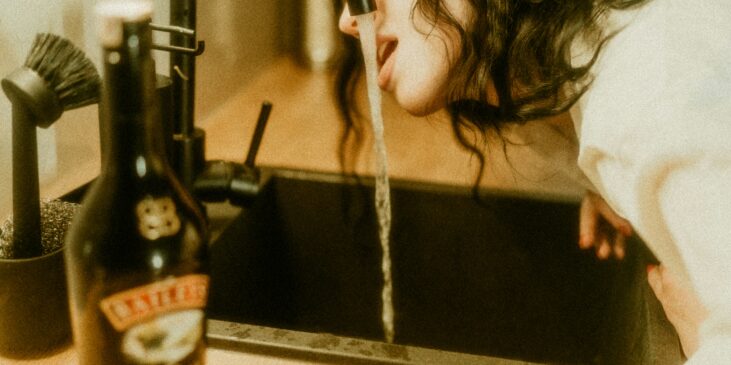 Frau, die Wasser aus einem Wasserhahn trinkt, daneben eine unberührte Flasche Alkohol