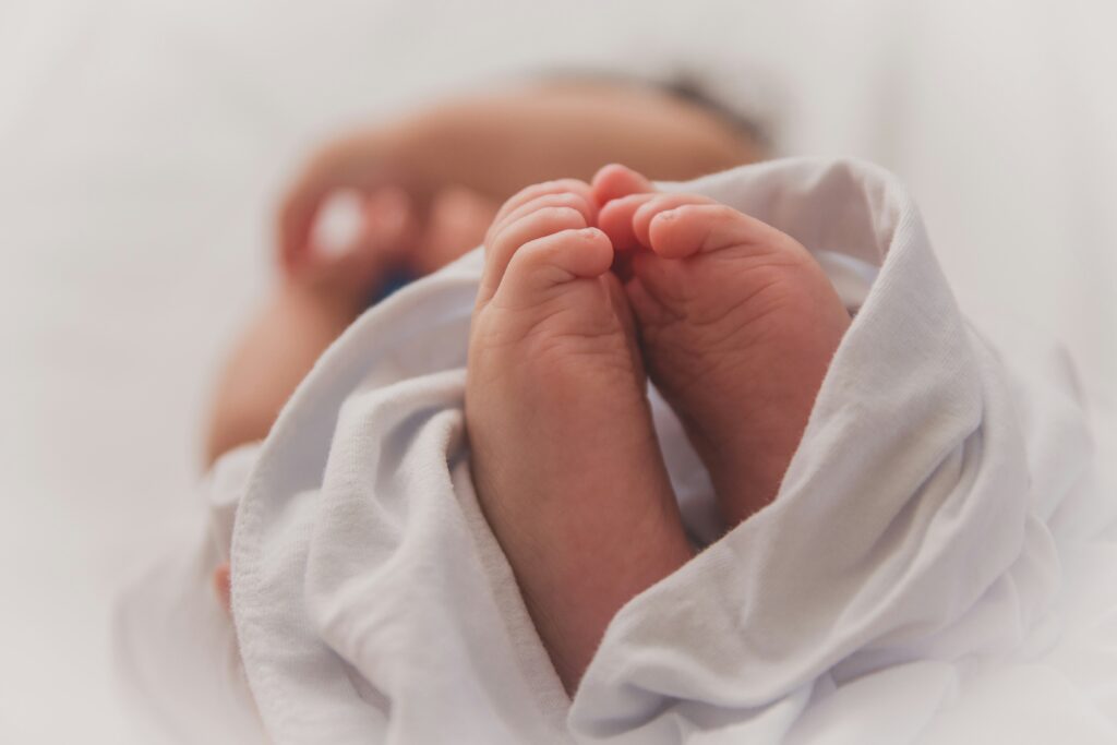Kleine Füße und Hände eines Babys in weißem Stoff eingewickelt