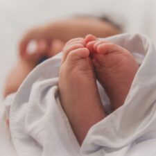 Kleine Füße und Hände eines Babys in weißem Stoff eingewickelt