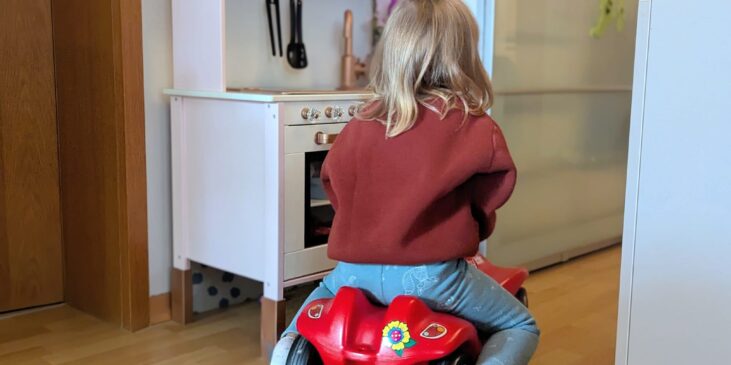 Kleinkind fährt mit einem roten Bobbycar durch die Wohnung.