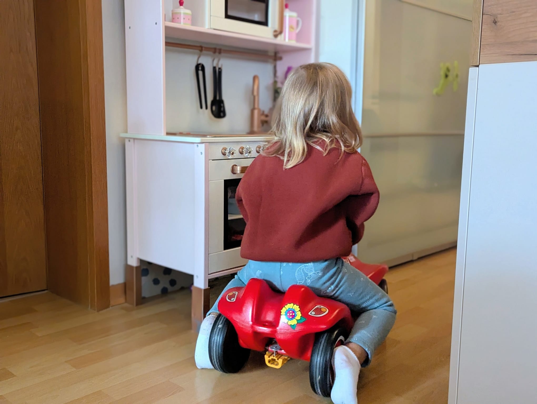 Kleinkind fährt mit einem roten Bobbycar durch die Wohnung.