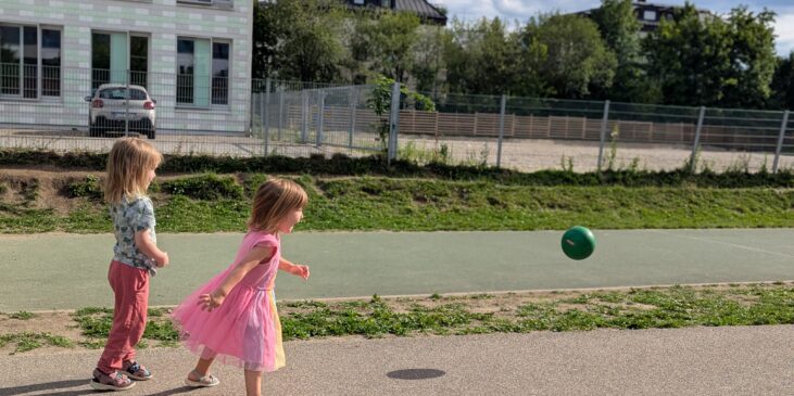 Zwei Kleinkinder laufen draußen einem Ball hinterher.