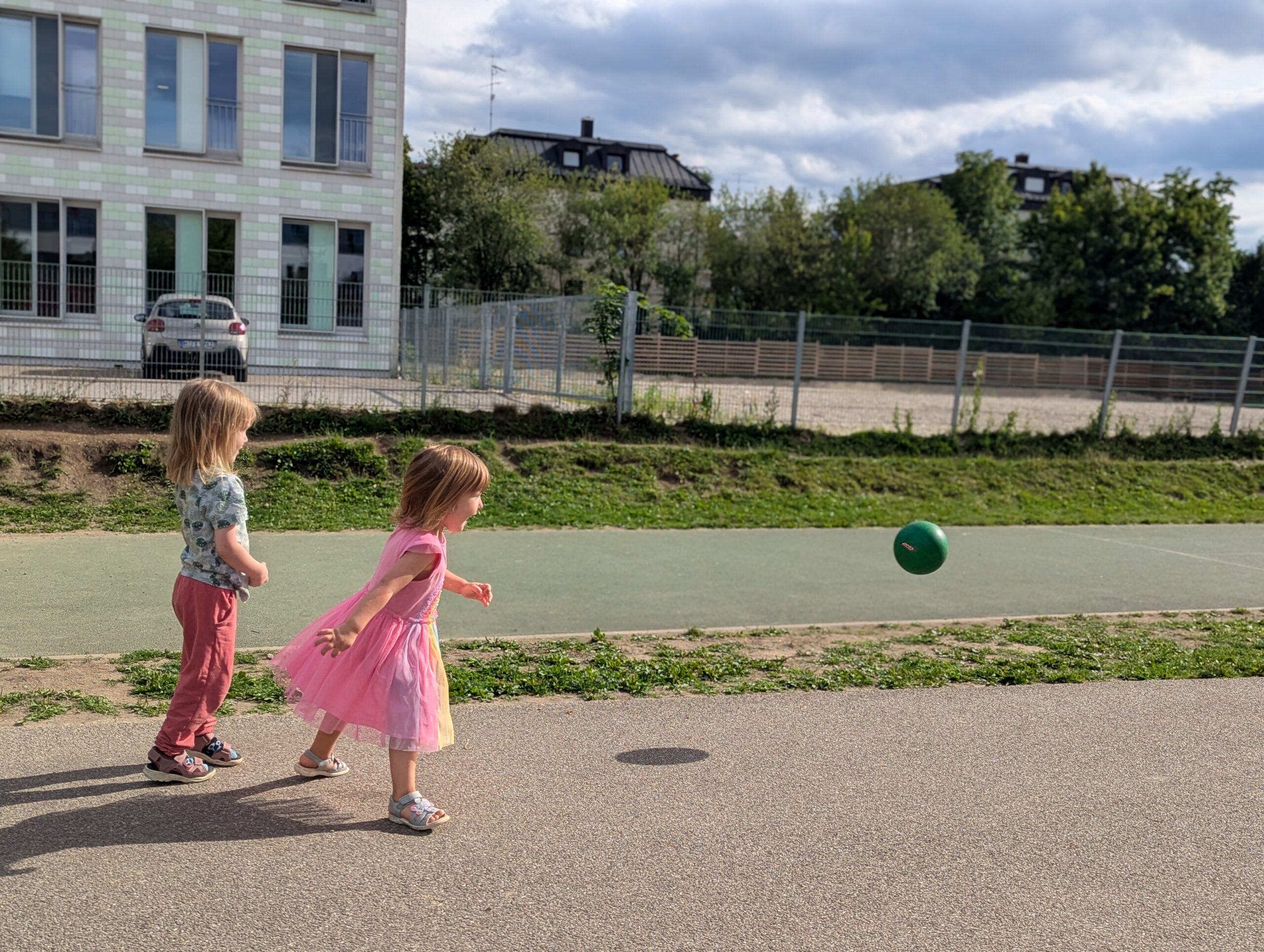 Zwei Kleinkinder laufen draußen einem Ball hinterher.