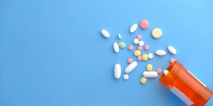 Pillen und offene Pillendose auf blauem Hintergrund