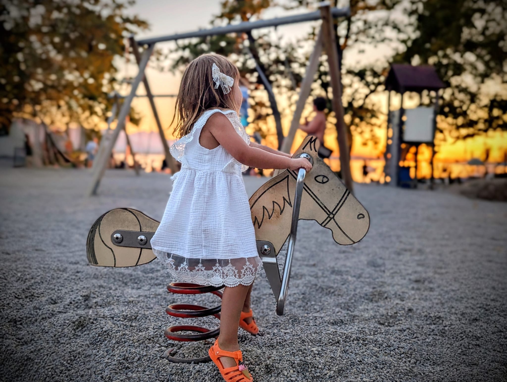 Kleines Mädchen spielt auf einer Wippe auf dem Spielplatz bei Sonnenuntergang.