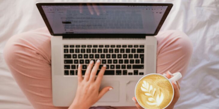 Frau sitzt mit Kaffee und Laptop im Bett
