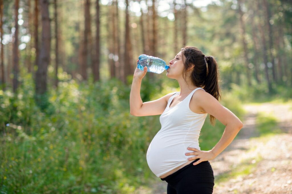 Schwangere Frau trinkt Wasser im Freien nach dem Training