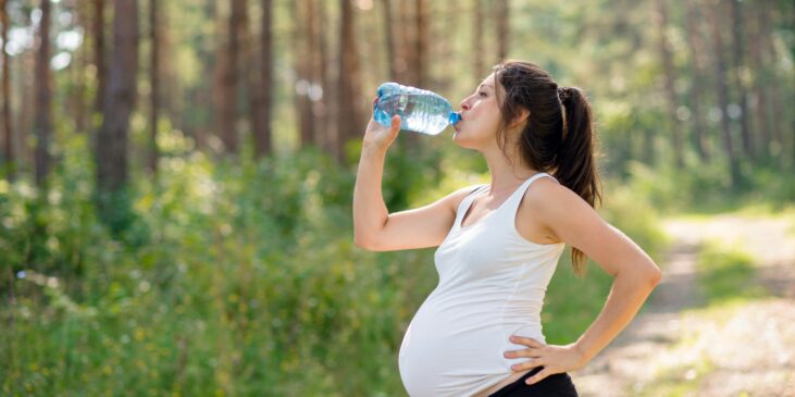 Schwangere Frau trinkt Wasser im Freien nach dem Training