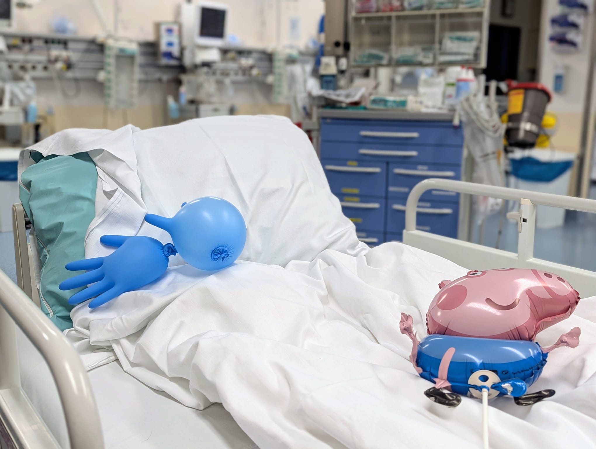 Leeres Krankenhausbett im Aufwachraum mit einem Luftballon und aufgeblasenen OP-Handschuhen.