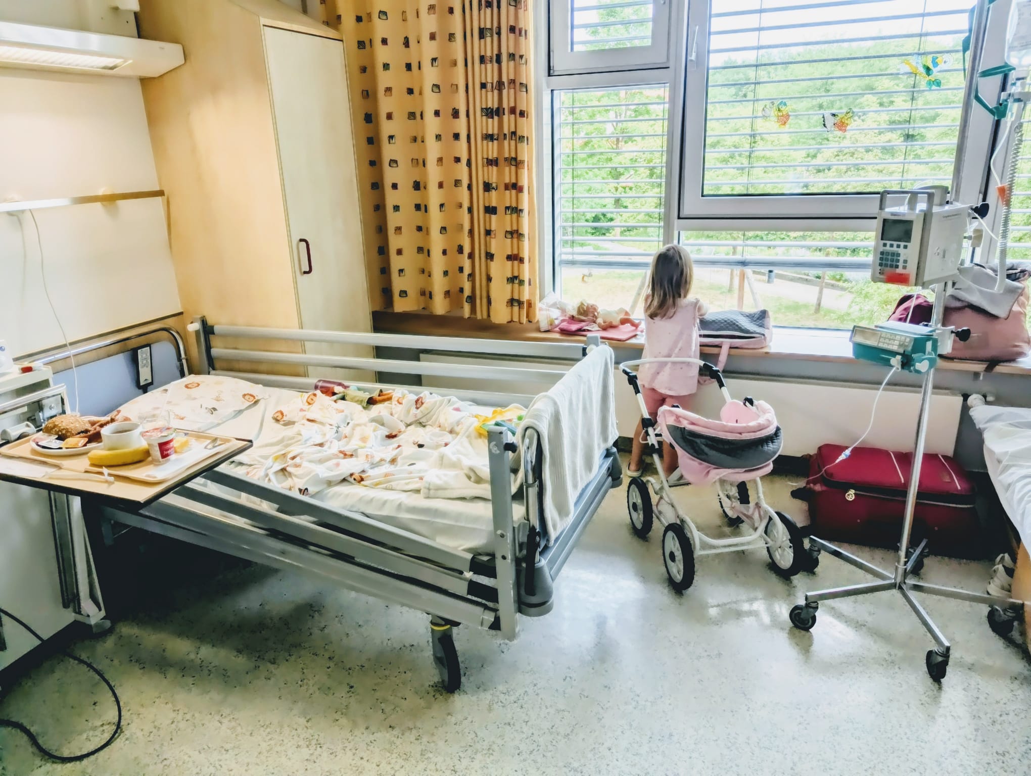 Kleinkind spielt im Krankenzimmer der Kinderklinik mit Puppe und Puppenwagen.