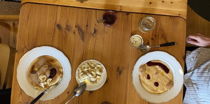 Tisch mit Milchreis in mehreren Schüsseln, Bananen, Marmelade und weiteren Frühstückszutaten in einer gemütlichen Berghütte.