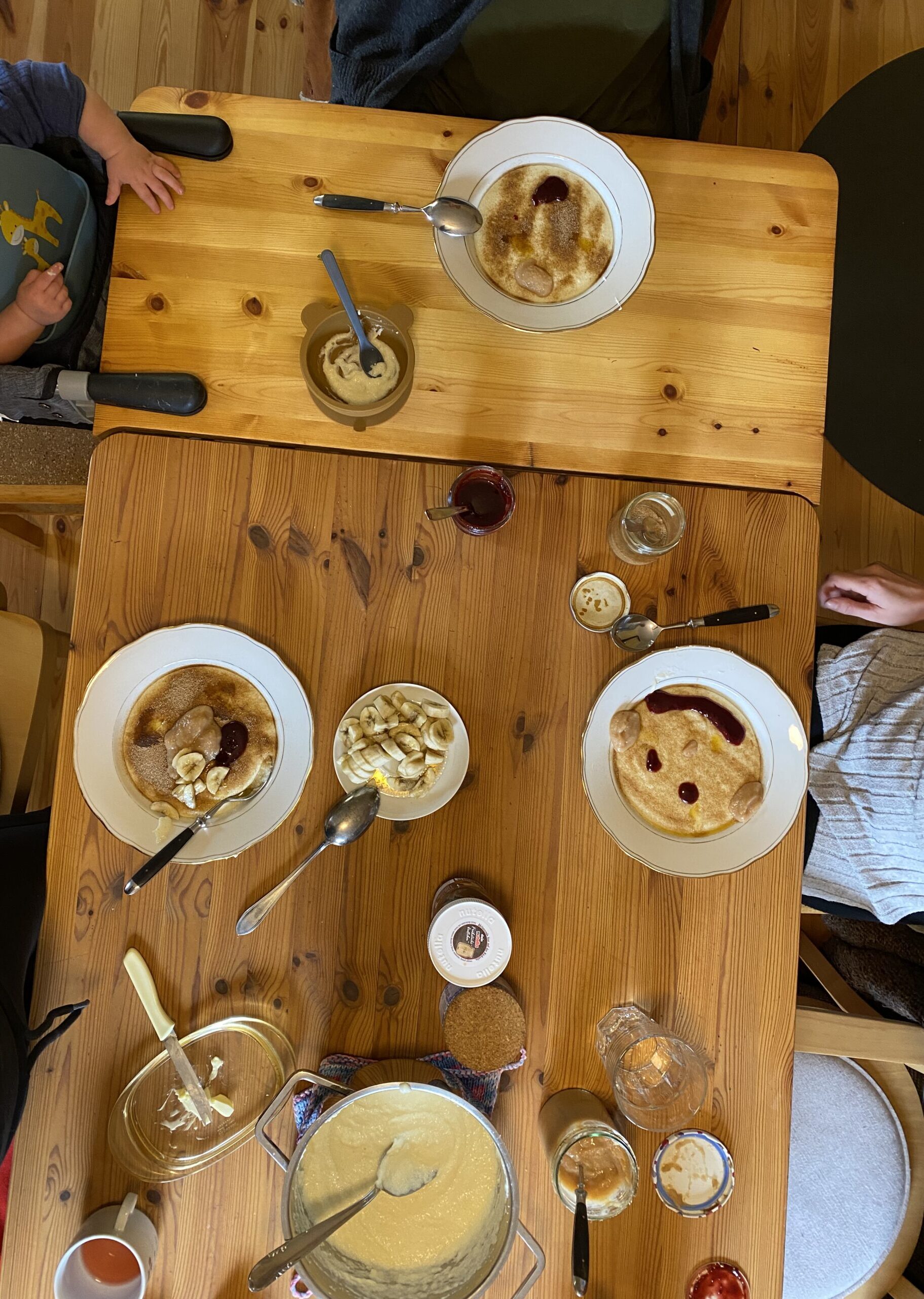 Tisch mit Milchreis in mehreren Schüsseln, Bananen, Marmelade und weiteren Frühstückszutaten in einer gemütlichen Berghütte.